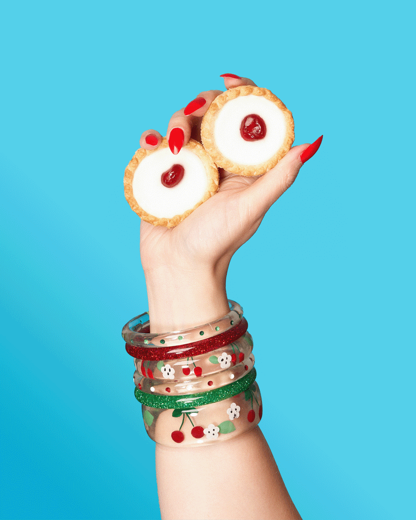 Splendette vintage inspired 1950s rockabilly style Cherries Clear Bangles with red and green glitters modelled by a hand crushing Bakewell tarts