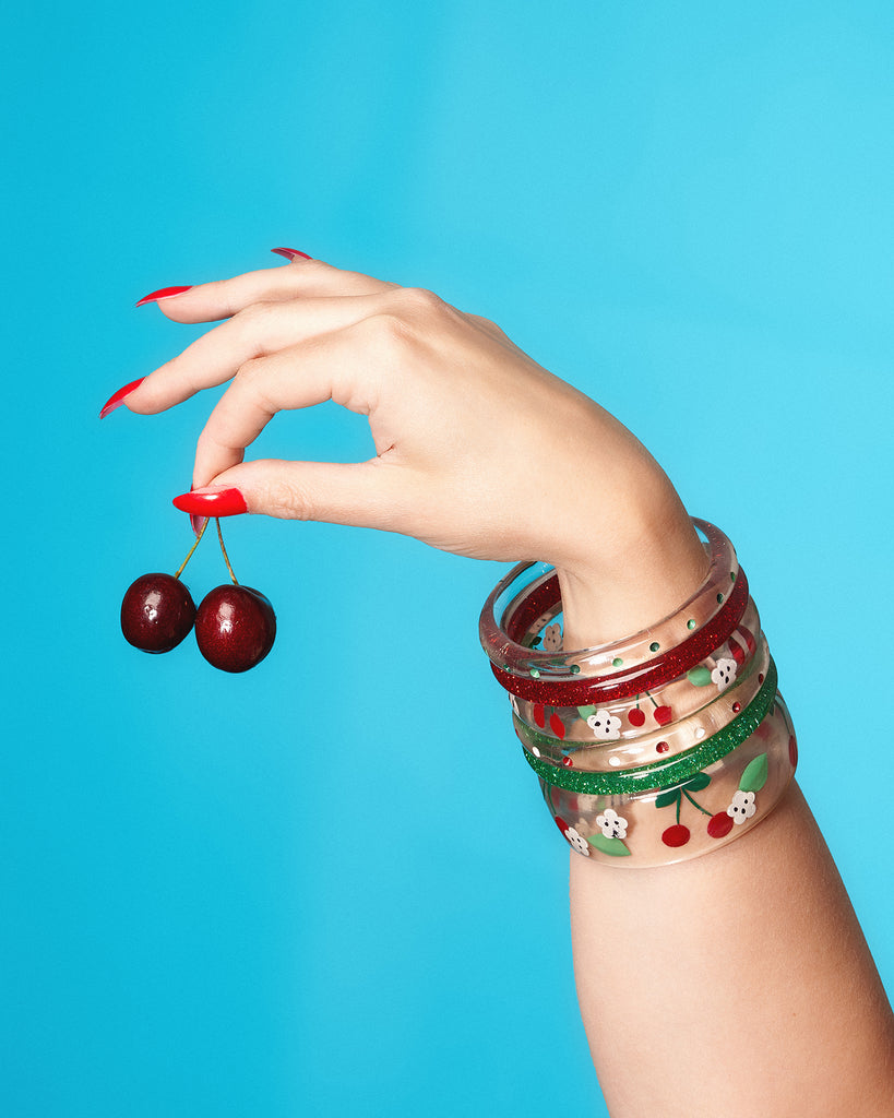Splendette vintage inspired 1950s rockabilly style Cherries Clear Bangles with red and green glitters modelled by a hand holding cherries