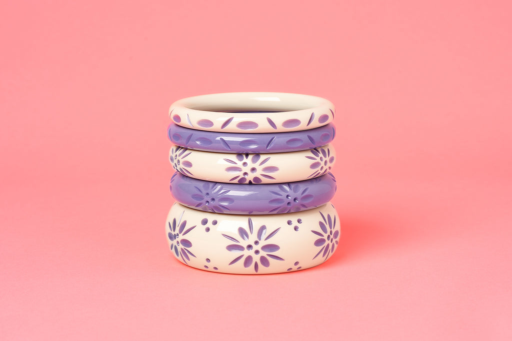Splendette vintage inspired 1940s style pastel purple carved fakelite Petunia and Cream Petunia Bangles on a pink background